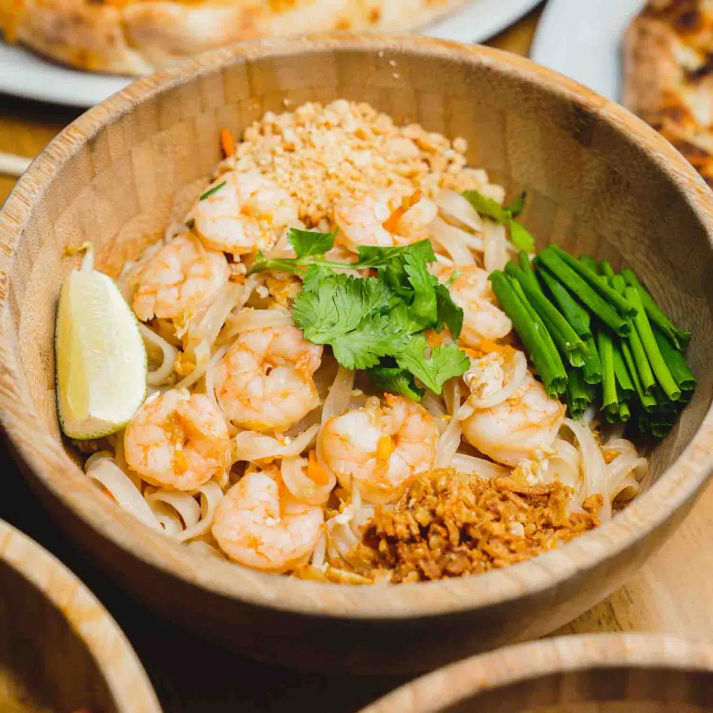 Pad thaï aux crevettes, ciboulette et citron dans un bol en bois