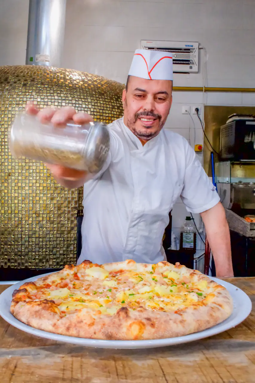 Pizzaiolo de La Trattoria saupoudrant une pizza napolitaine